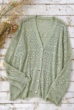 Load image into Gallery viewer, Green knitted cardigan on a wooden surface with dried plants.