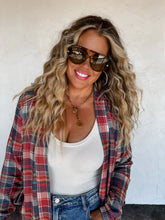 Load image into Gallery viewer, Woman wearing sunglasses, a plaid shirt, and a white top against a white wall.
