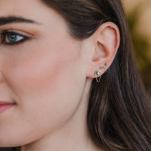 Load image into Gallery viewer, Close-up of a woman&#39;s ear wearing gold earrings with green gemstones.