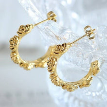 Load image into Gallery viewer, Gold hoop earrings with intricate designs on a clear stand against a light background