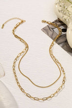 Load image into Gallery viewer, Gold chain necklace on a textured white surface with a blurred decorative object in the background.