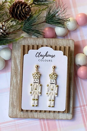 Nutcracker-shaped earrings on a Clayhouse Colours card with Christmas decorations in the background.