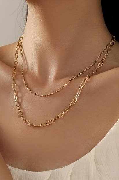 Gold chain necklace on a person's neck with a neutral background