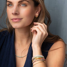 Load image into Gallery viewer, Woman wearing gold earrings and bracelets against a gray background