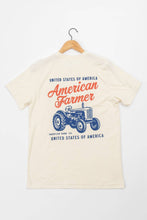 Load image into Gallery viewer, Beige t-shirt with 'American Farmer' graphic on a hanger against a white background