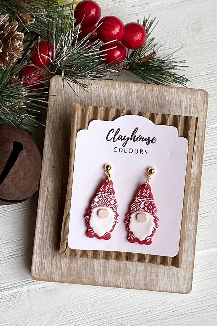 Red gnome-shaped earrings on a 'Clayhouse Colours' card with Christmas decorations.