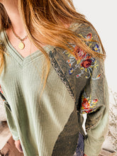 Load image into Gallery viewer, Close-up of a person wearing a green ribbed sweater with floral embroidery on the sleeves.
