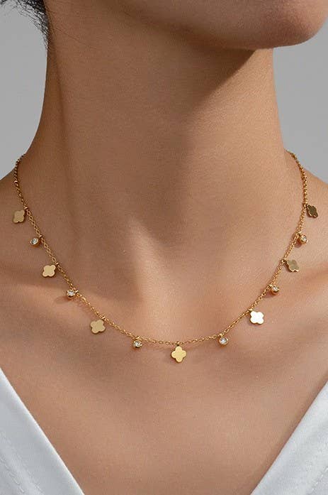 Gold necklace with small pendants on a person wearing a white top against a neutral background