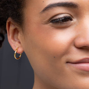 Close-up of a person wearing a gold hoop earring against a neutral background