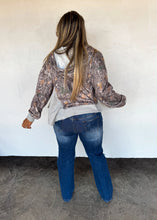 Load image into Gallery viewer, Person wearing a patterned hoodie and blue jeans against a white wall.