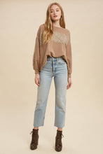 Load image into Gallery viewer, Woman wearing a brown sweater with lace detail and light blue jeans on a beige background