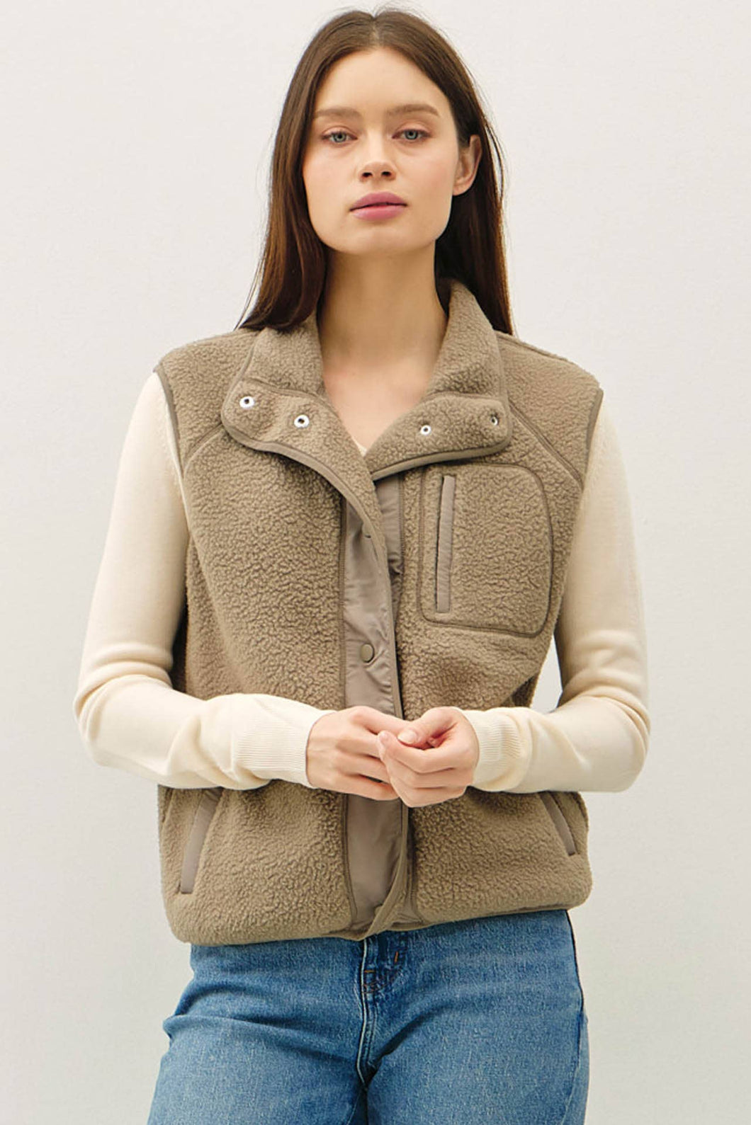 Woman wearing a beige fleece vest over a cream sweater with a white background