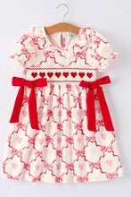 Load image into Gallery viewer, Children's dress with heart and bow pattern on a hanger against a white background