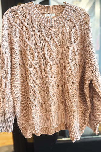 Beige cable knit sweater on a mannequin against a blurred indoor background