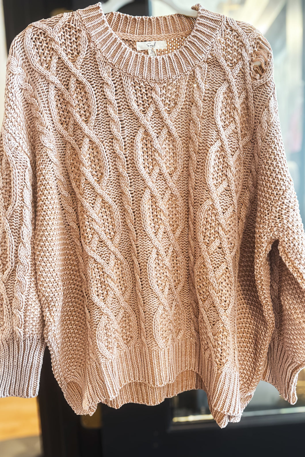 Beige cable knit sweater on a mannequin against a blurred indoor background