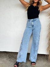 Load image into Gallery viewer, Person wearing high-waisted light blue jeans and a black top against a white wall.