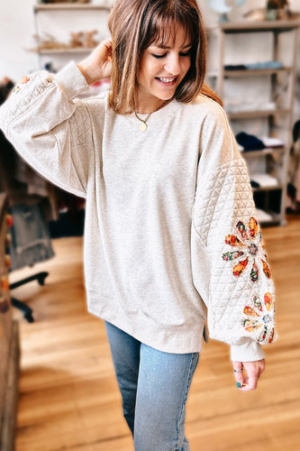 girl wearing grey sweatshirt with quilted sleeves and floral patches