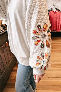 girl wearing grey sweatshirt with quilted sleeves and floral patches, close up