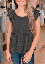 Load image into Gallery viewer, Woman wearing a dark gray ruffled top and jeans in a clothing store.