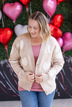 Load image into Gallery viewer, Woman wearing a beige cardigan with heart patterns in front of heart-shaped balloons.