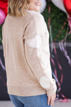 Load image into Gallery viewer, Person wearing a beige sweater with heart patterns in front of balloons and streamers.