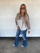 Load image into Gallery viewer, Woman wearing a floral top and blue jeans against a white wall.