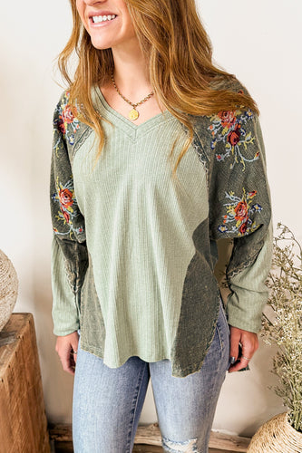 Woman wearing a green floral-patterned top and jeans standing in a home setting with decorative elements.