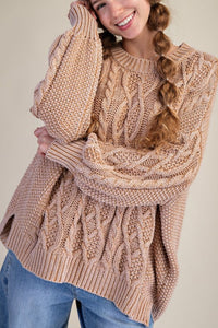Woman wearing a beige cable knit sweater with a plain background