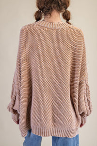 Person wearing a beige knitted sweater and blue jeans on a plain background