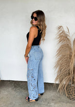 Load image into Gallery viewer, Woman wearing light blue jeans and a black top standing against a white wall with pampas grass.