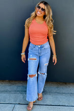Load image into Gallery viewer, Woman wearing a coral top and blue jeans standing against a dark wall.