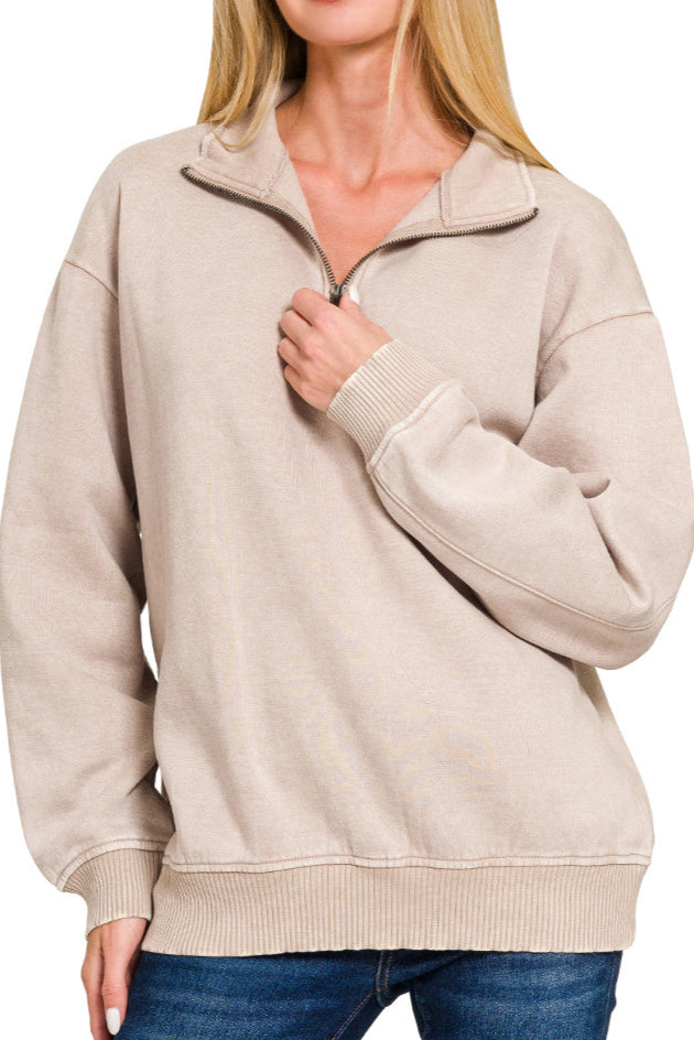 Woman wearing a beige half-zip sweatshirt with blue jeans on a white background