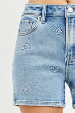 Load image into Gallery viewer, Blue denim shorts with floral embroidery on a light gray background