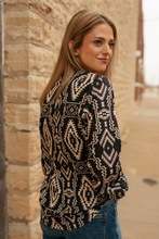 Load image into Gallery viewer, Woman wearing a black and beige patterned cardigan against a stone wall.
