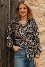Load image into Gallery viewer, Woman wearing a black and white patterned blouse against a stone wall.