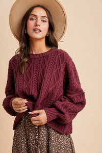 Woman wearing a maroon cable knit sweater and beige hat on a beige background