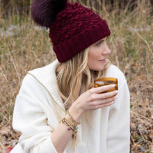 Load image into Gallery viewer, Woman in a red knit hat and white coat holding a wooden mug outdoors.
