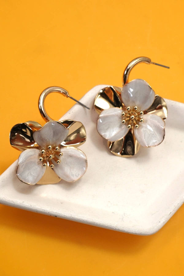 Floral earrings with gold accents on a white dish against an orange background