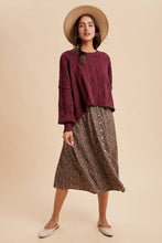 Load image into Gallery viewer, Woman wearing a burgundy cable knit sweater and patterned skirt with a beige hat on a beige background