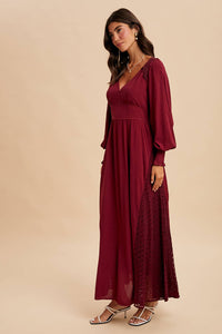 Woman wearing a burgundy long-sleeve dress with lace details on a beige background