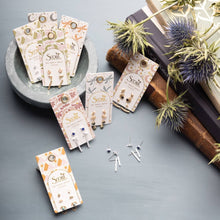 Load image into Gallery viewer, Scout earrings on display with packaging and decorative elements on a gray surface