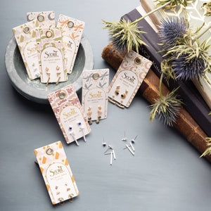 Scout earrings on display with packaging and decorative elements on a gray surface