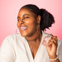 Load image into Gallery viewer, Woman holding a perfume bottle against a pink background
