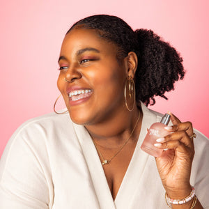 Woman holding a perfume bottle against a pink background