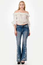 Load image into Gallery viewer, Woman wearing a white off-shoulder top and blue jeans with floral embroidery on a white background