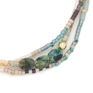 Multistrand beaded necklace with green stones and gold accent on a white background