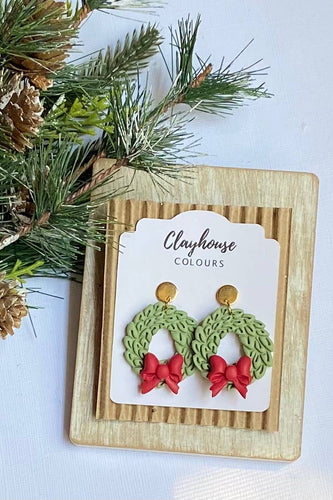 Pair of green and red earrings on a 'Clayhouse Colours' branded card with Christmas decorations.