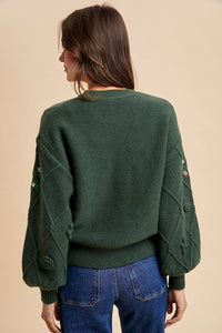 Person wearing a green sweater with embroidered details on a beige background