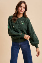 Load image into Gallery viewer, Woman wearing a green sweater with floral embellishments on a beige background