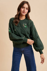 Woman wearing a green sweater with floral embellishments on a beige background